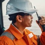 Filipino deck Officer on deck of vessel or ship , wearing PPE personal protective equipment. He speaks to VHF walkie-talkie radio in hands. Dream work at sea