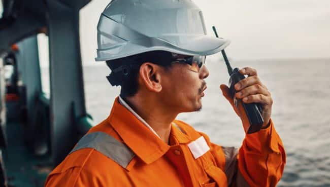 Filipino deck Officer on deck of vessel or ship , wearing PPE personal protective equipment. He speaks to VHF walkie-talkie radio in hands. Dream work at sea