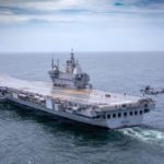 Indegenious aircraft carrier Vikrant sailing out for sea trials, with a helicopter hovering above it