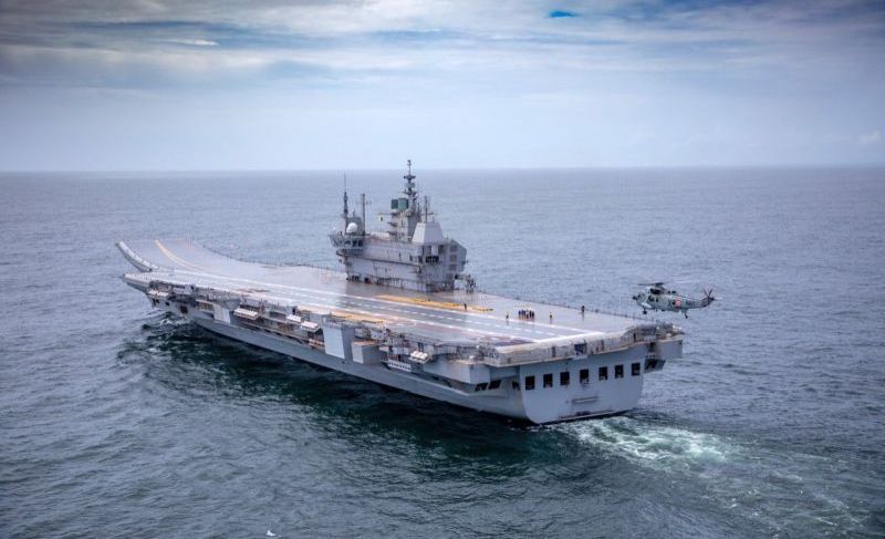 Indegenious aircraft carrier Vikrant sailing out for sea trials, with a helicopter hovering above it